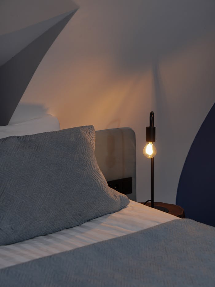 A serene bedroom with a glowing bulb lamp casting shadows, creating a cozy ambiance.